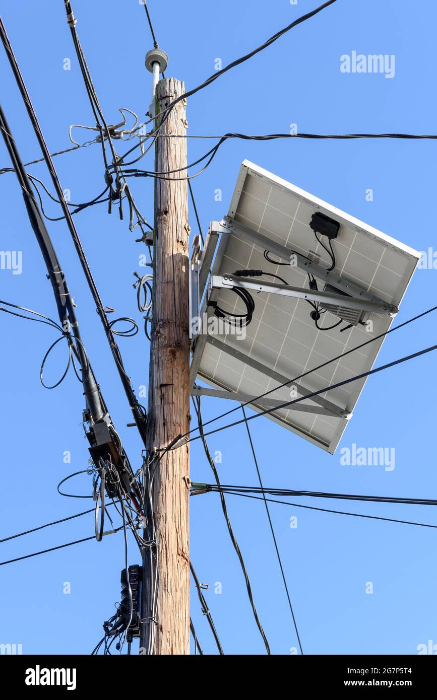 Multiple phone, electric and cable wiring, all disorganized, on a pole with a large solar panel. Stock Photo