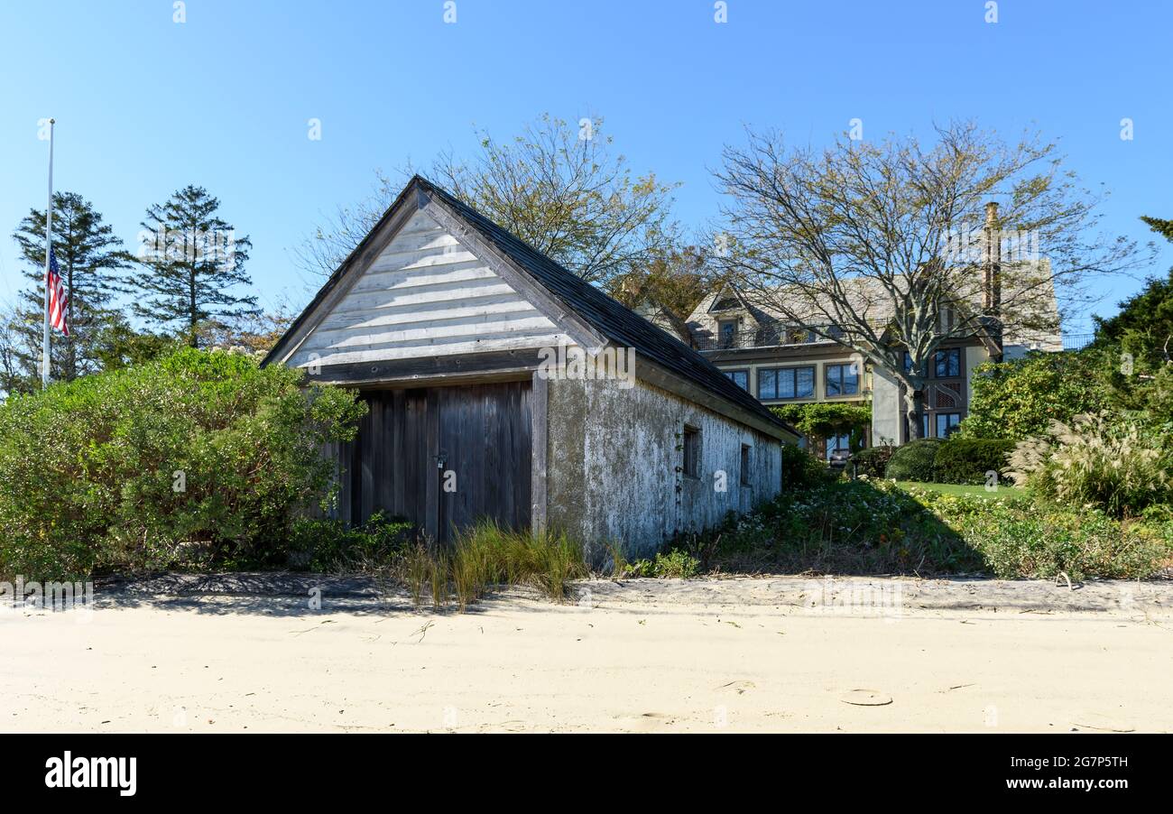 A boat house on the coast with sand in front, and an estate home in the background. Stock Photo