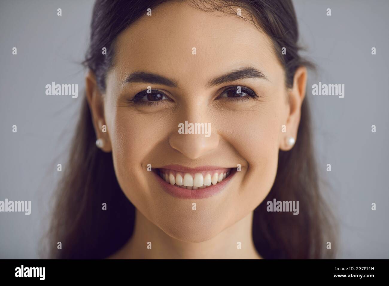Head shot of happy young woman with long dark hair and friendly open smile looking at camera Stock Photo