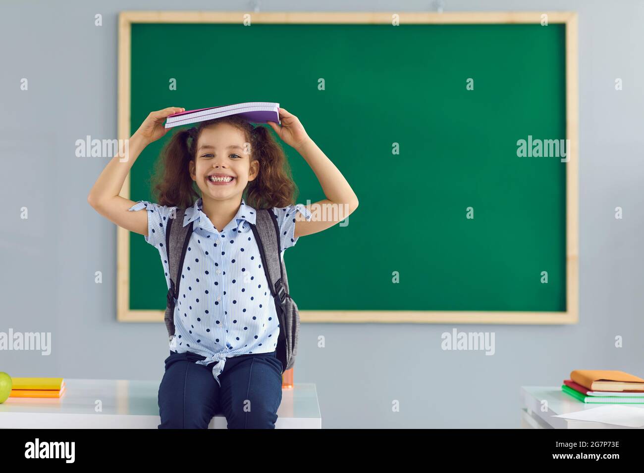 Concept back to school. Happy schoolgirl holds a book over her head ...