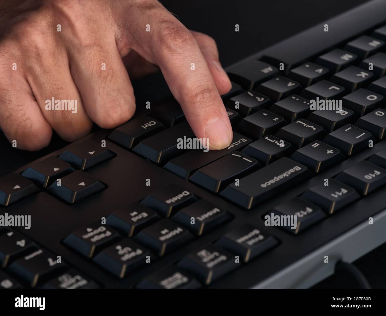 A person pressing the enter key on a black keyboard. Close up. Low key Stock Photo