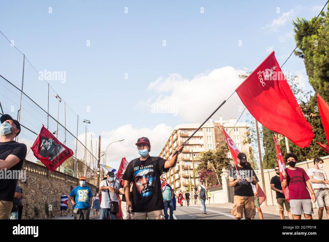 Barcelona, Spain. 15th July, 2021. A protester wearing a shirt with the face of Ernesto Che Guevara holds a communist flag during the demonstration.About a hundred people have demonstrated against the United States blockade against Cuba in front of the US consulate in Barcelona. Credit: SOPA Images Limited/Alamy Live News Stock Photo