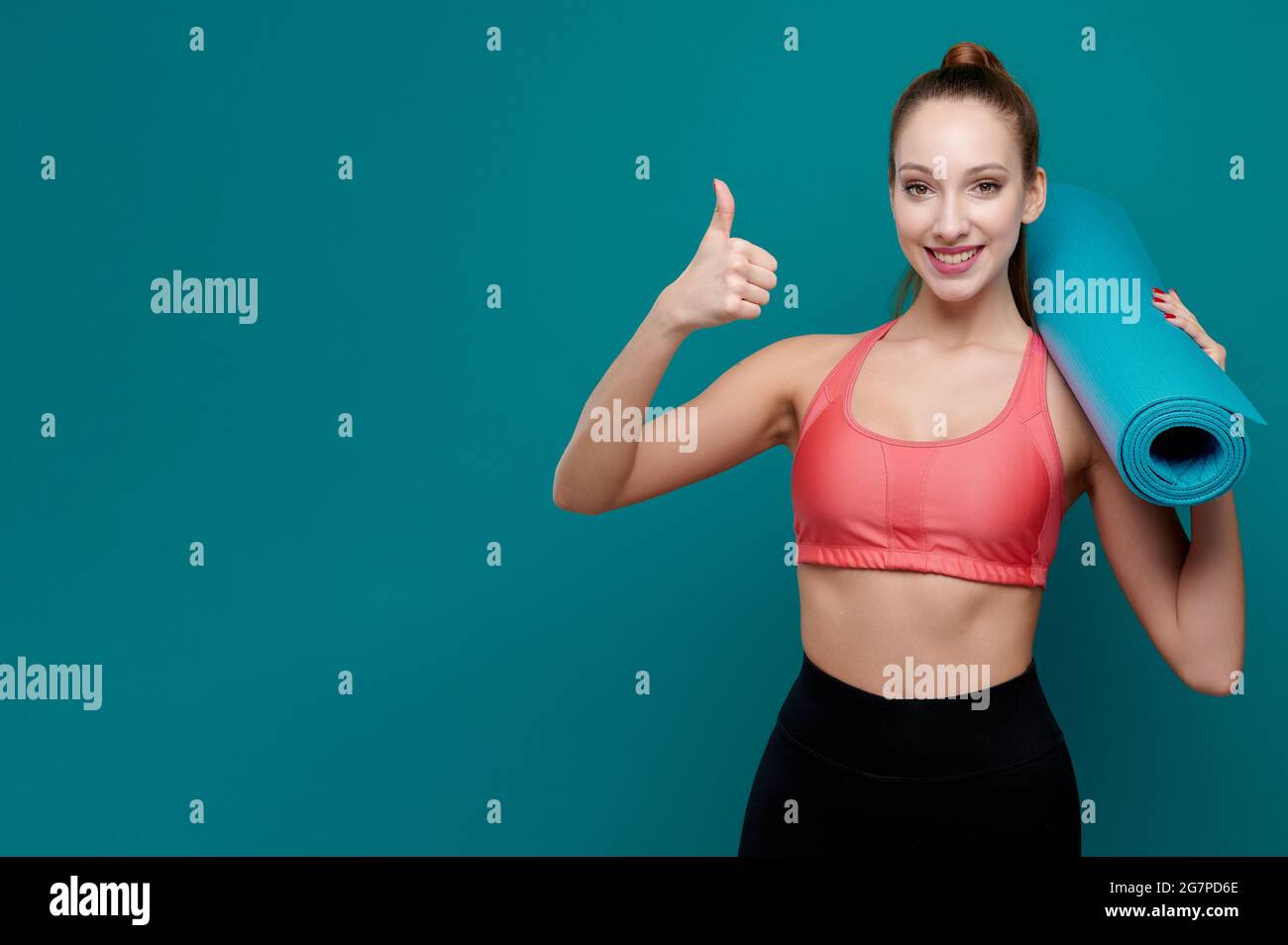 Young sporty smiling woman in sportswear holding yoga mat in her hands ...