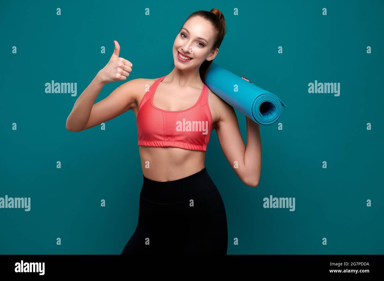 Young sporty smiling woman in sportswear holding yoga mat in her hands ...