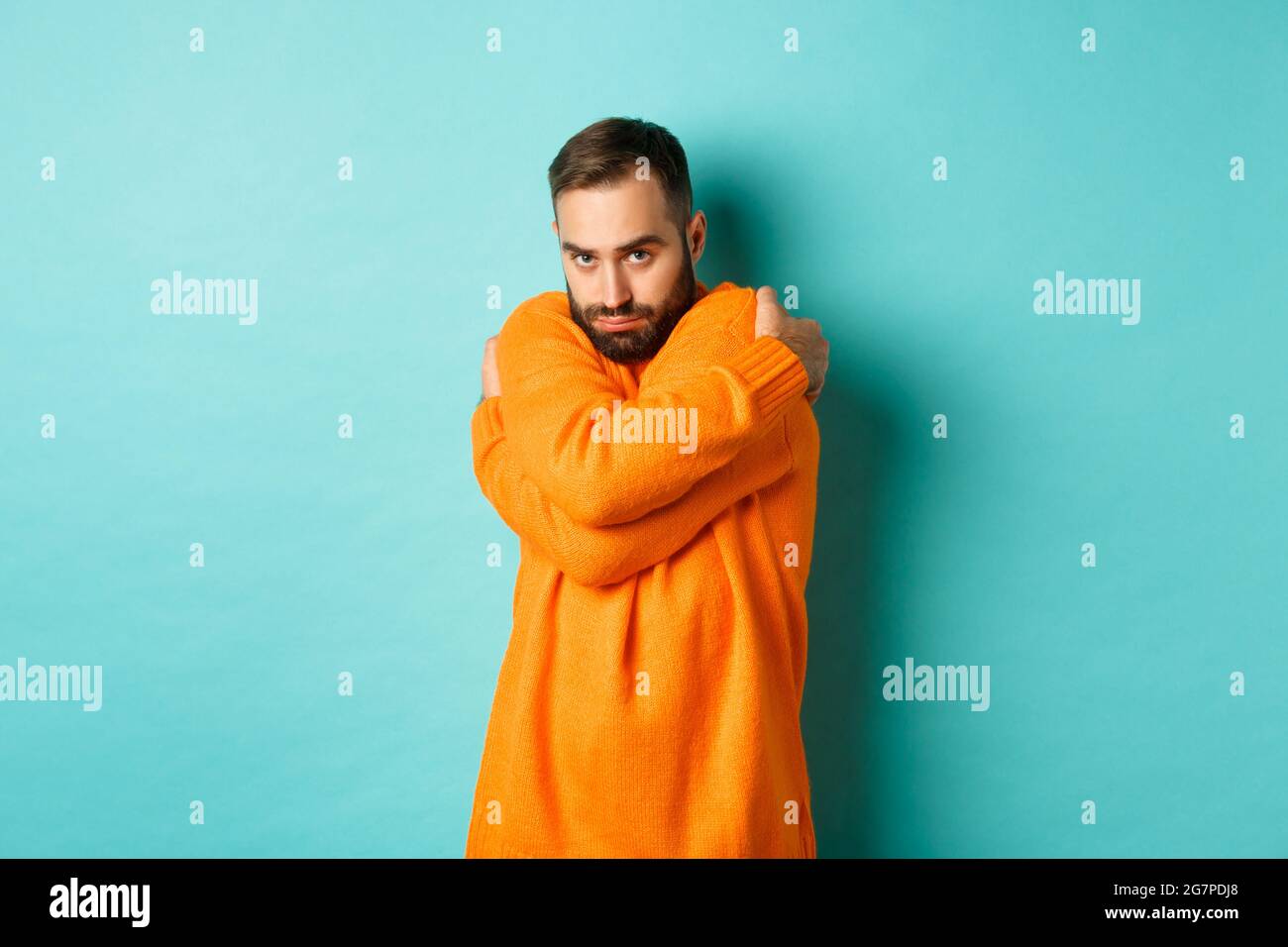 Timid man feeling offended and defensive, hugging himself and looking suspicious at camera, standing over light blue background Stock Photo