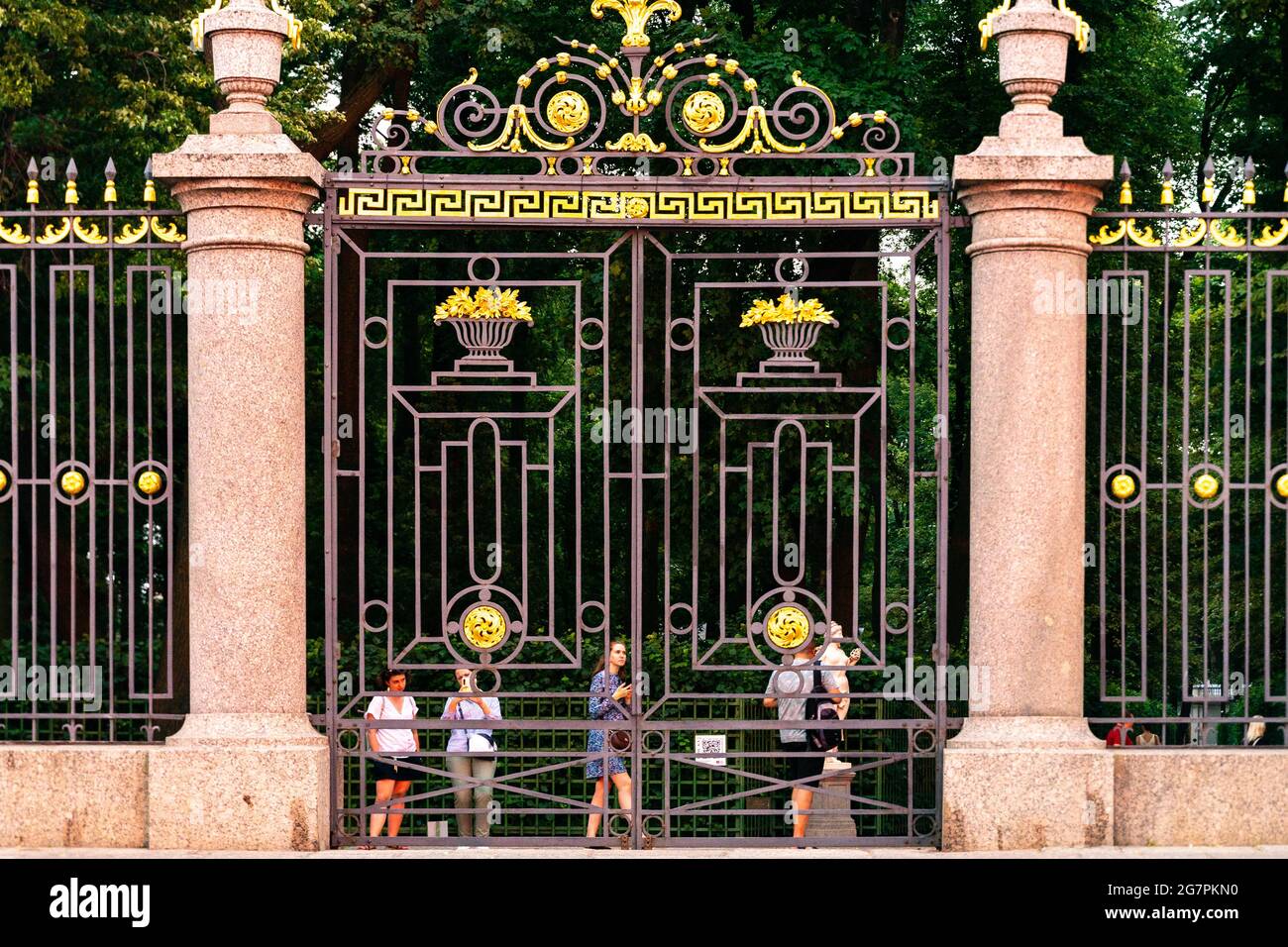 Visitors look through massive iron gate of Summer garden on Kutuzovskaya embankment, white nights, St Petersburg, Russia Stock Photo