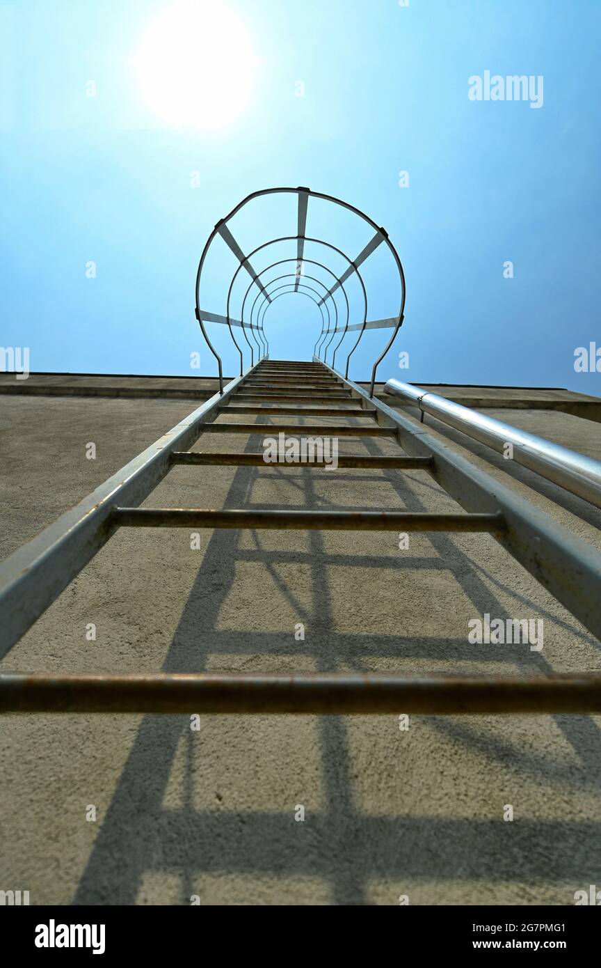 Vertical low angle of metal escape ladder on a concrete wall under blue