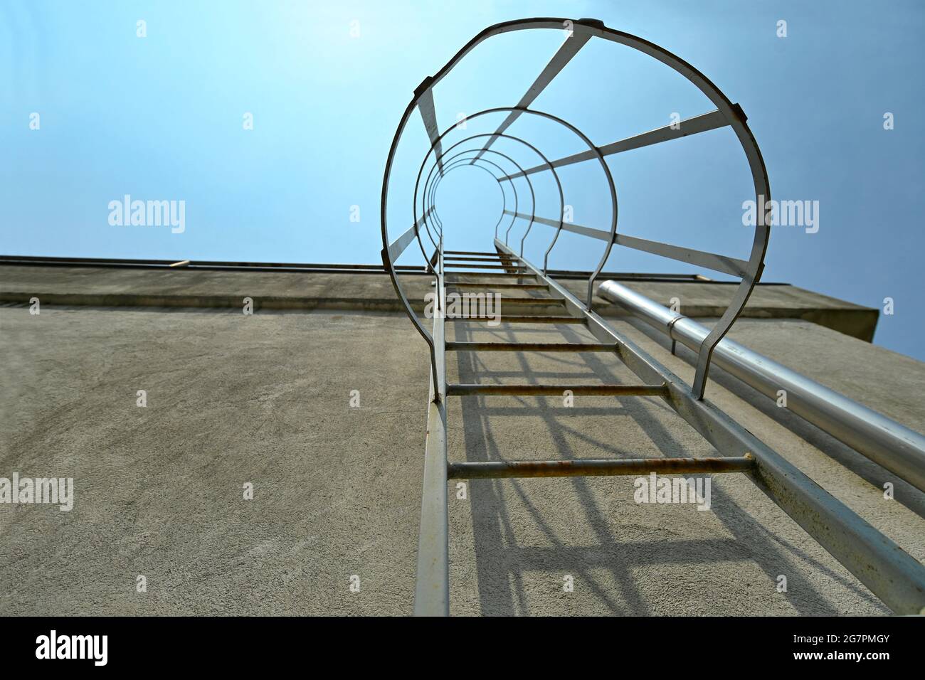 Low angle of metal escape ladder on a concrete wall under blue sky