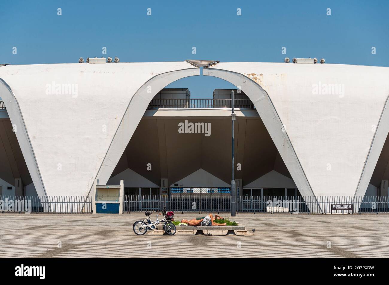 People sunbath in the plaza, the athletics stadium in the background, used during the 1964 Tokyo Olympics, and stands inside Komazawa Olympic Park, Tokyo on 10 June 2021.  Robert Gilhooly photo Stock Photo