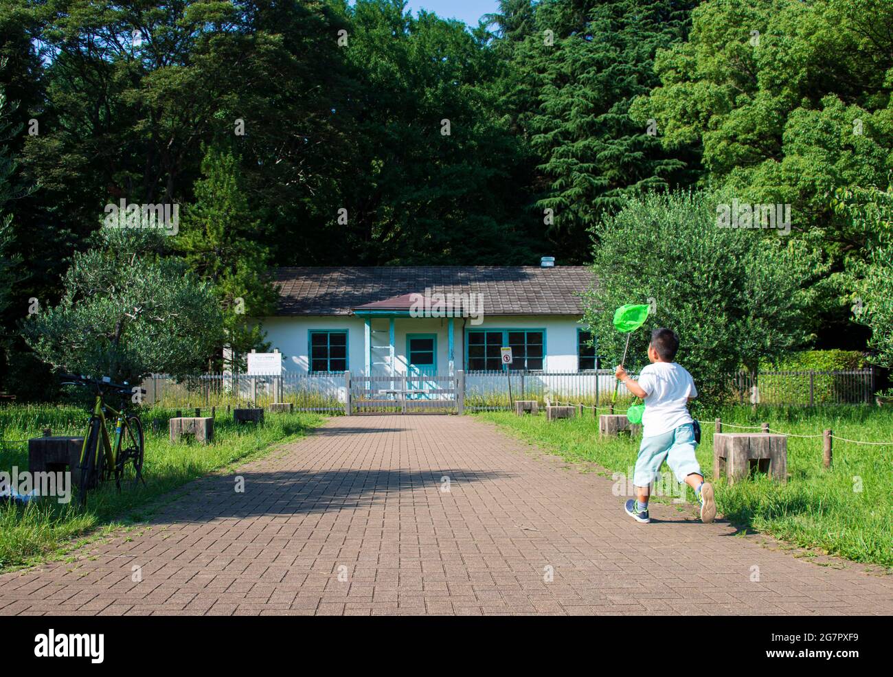 A boy chases after a butterfly in front of the only surviving structure from the athletes' village, which was used by team Netherlands during the 1964 Tokyo Olympics, and stands inside today's Yoyogi Park, Tokyo on 21 June 2021.  Robert Gilhooly photo Stock Photo
