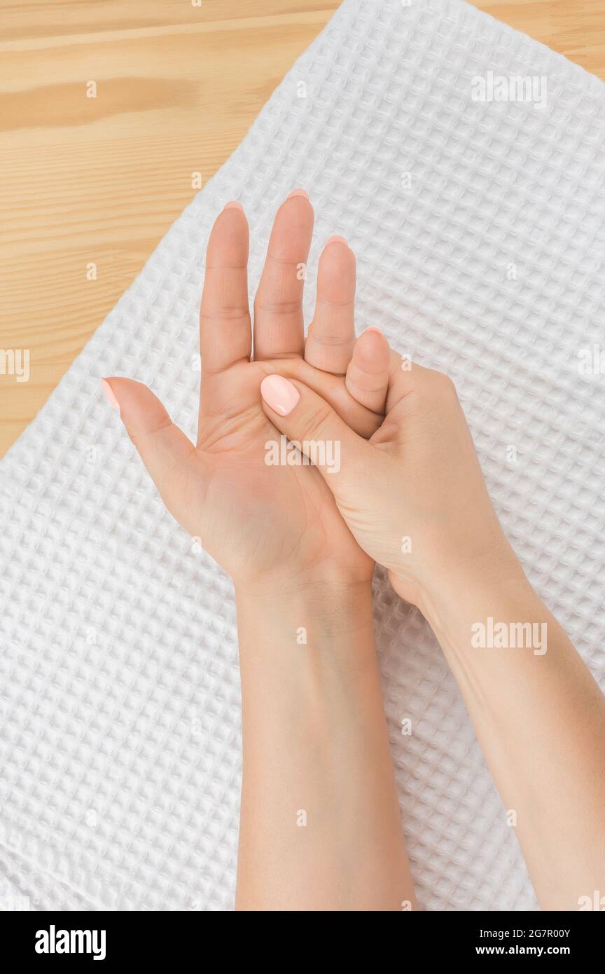 one female hand massages the other hand lying on a white towel with the open palm up. vertical image. Closeup hand of person massage her hand from pai Stock Photo