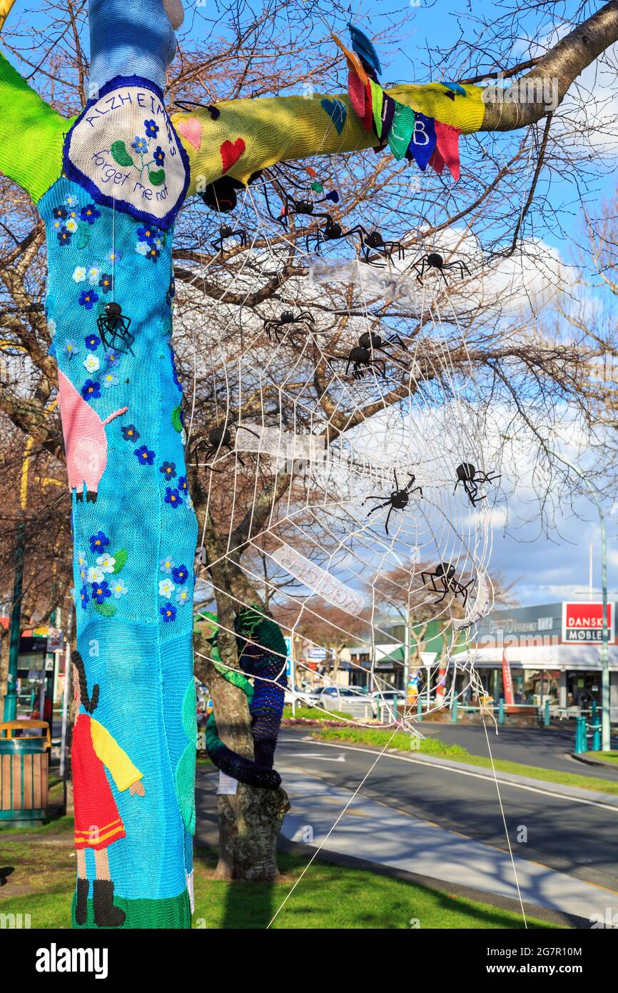'Yarn bombing', or knitted street art, on a tree. This example depicts the Alzheimers Society forget-me-not and a spider's web Stock Photo