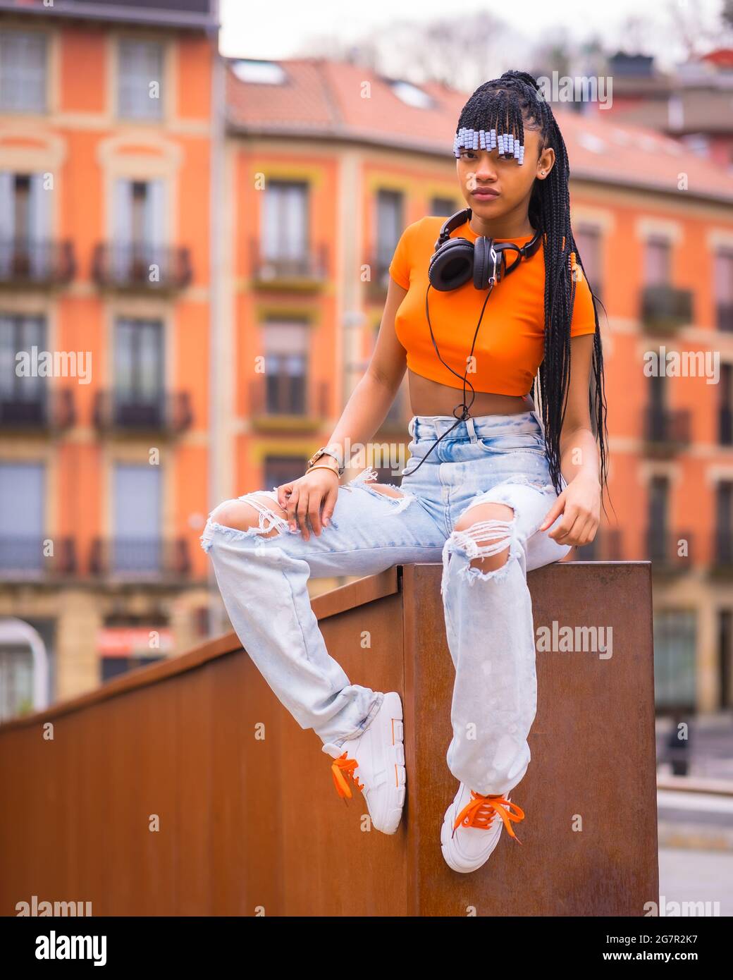 Native American trap dancer with braids wearing an orange shirt and cowboy pants sitting on the wall Stock Photo