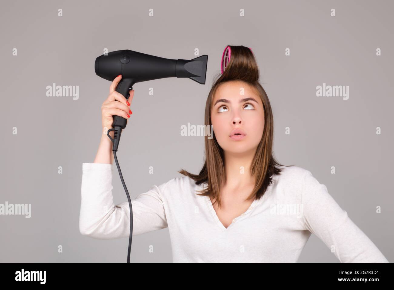 Woman with hair dryer. Funny girl with straight hair drying hair with professional hairdryer. Hairstyle, hairdressing concept. Stock Photo