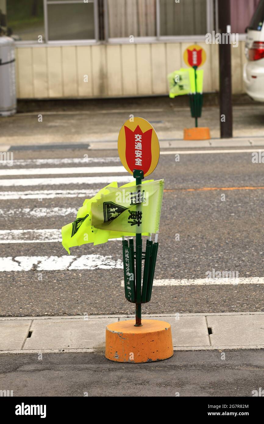 yellow Pedestrian crossing flags, with a street crosswalk ready for use at inawashiro lake. 'Crossing' is written on it in Japanese. Stock Photo