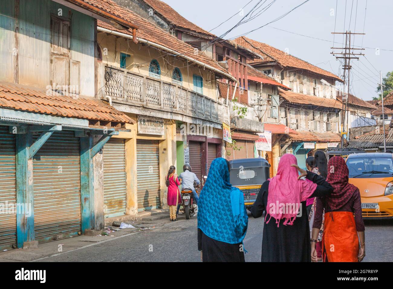 Rear view of muslim females wearing colourful shawls walking past rundown warehouses with closed shutters, Fort Kochi (cochin), Kerala, India Stock Photo