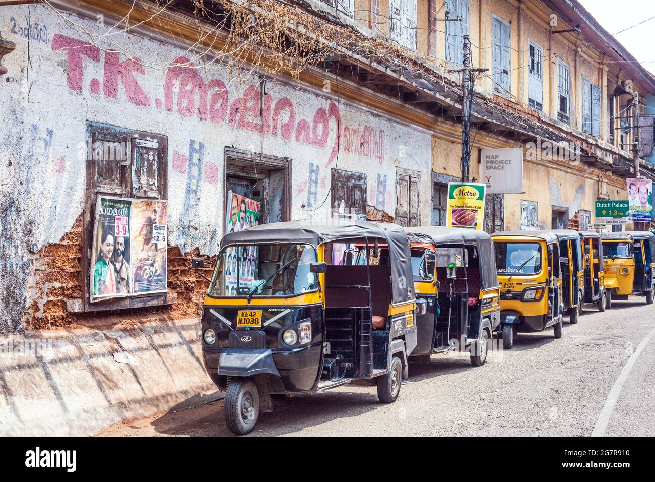 Row of auto rickshaws lined up in street outside warehouse with bollywood film poster on wall, Fort Kochi (cochin), Kerala, India Stock Photo