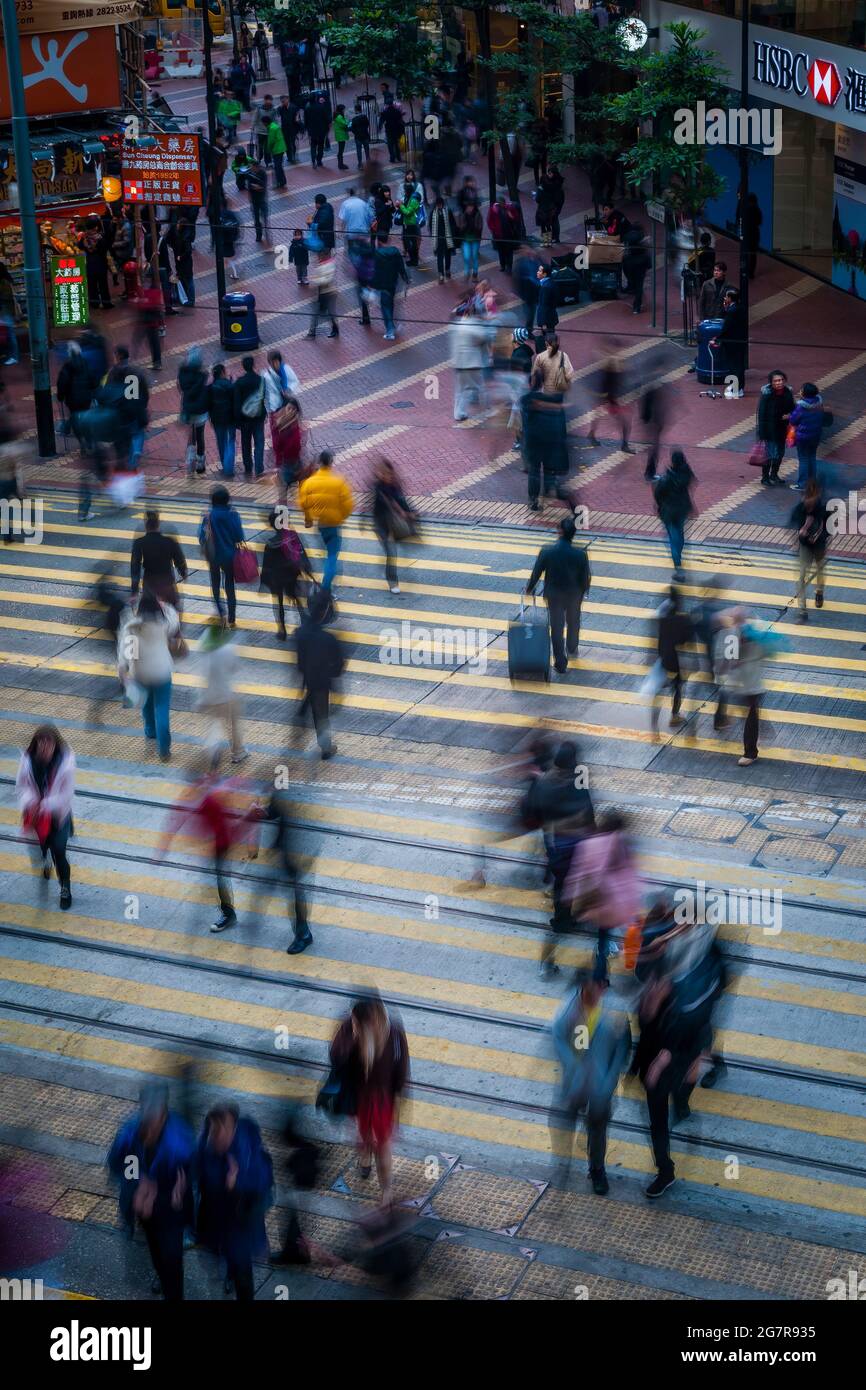 Pedestrians cross the tram tracks in Causeway Bay, Hong Kong Island, with blur effect from slow shutter speed Stock Photo