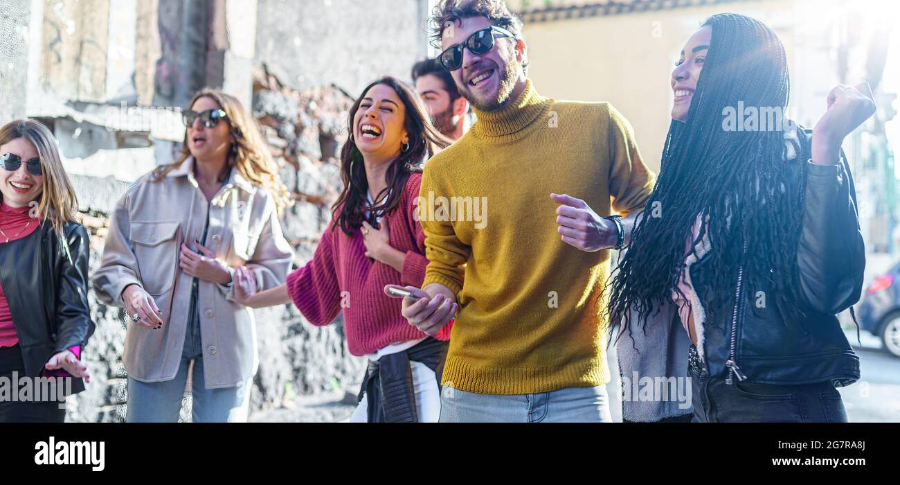 Group of young Friends gathering in the street listening music from smartphone and dancing together. Multiracial millennials having fun outdoors jokin Stock Photo