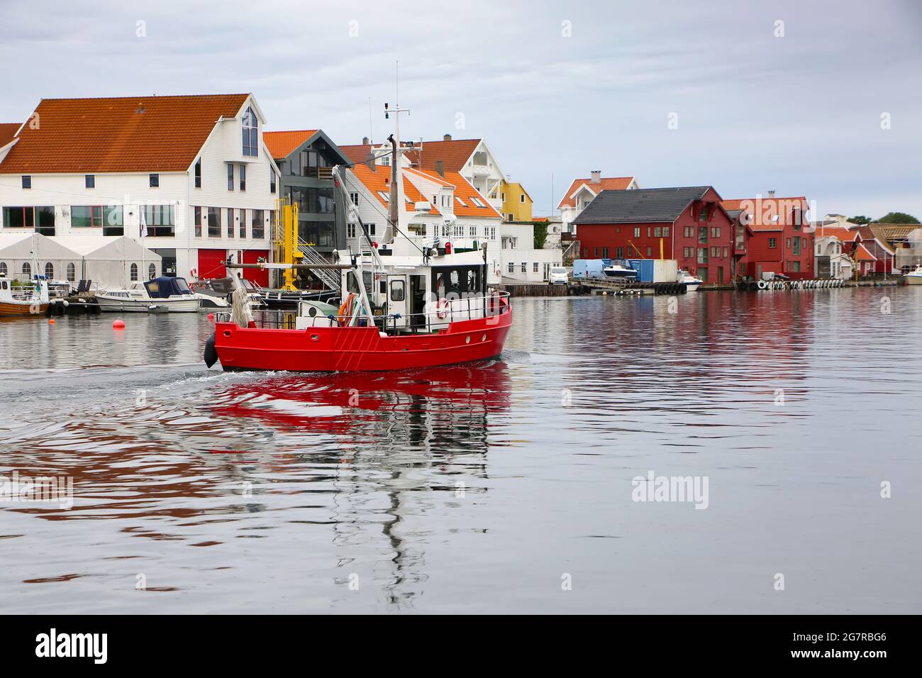Typical fishing boat with traditional wooden buildings along the waterfront, river, and the marina. Smedasundet, town centre, Haugesund, Norway. Stock Photo