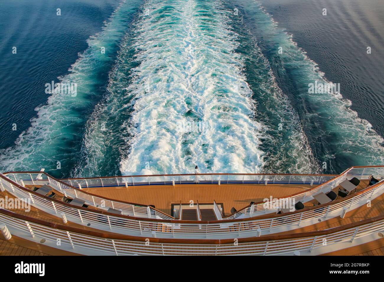 Looking down at the aft or back decks of a cruise ship and the wake or waves in the sea as it sails across the ocean. Open decks with tables & chairs Stock Photo