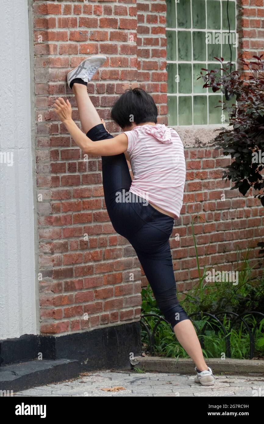 A nimble flexible young lady does rigorous stretching exercises in a park in New York City. Stock Photo