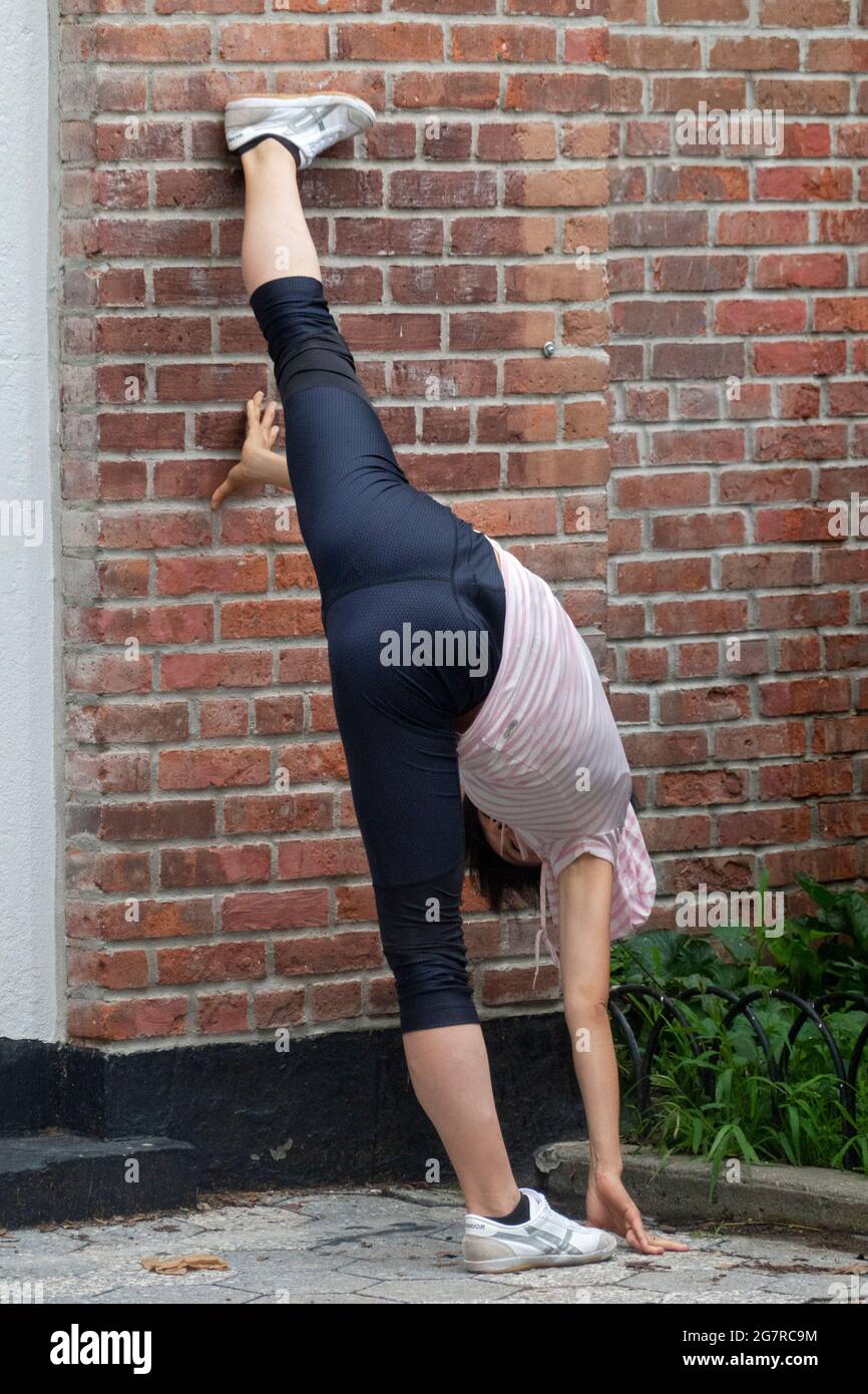 A nimble flexible young lady does rigorous stretching exercises in a park in New York City. Stock Photo