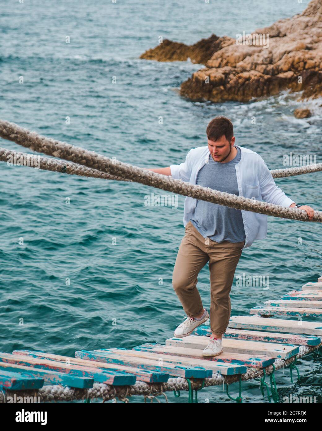 man walking by suspension bridge cross sea bay rocky cliff summer time ...