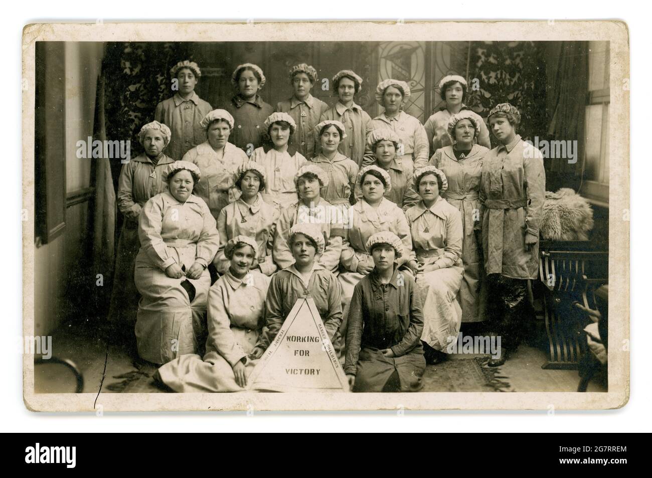 Original WW1 era  postcard notice reads 'Working for Victory' and around the edge is printed Royal Arsenal Danger Buildings Woolwich Arsenal. A group of women munitionettes wear on war service badges  circa 1916, 1917,  Arsenal was a shell filling factory. Woolwich, London, U.K. Stock Photo