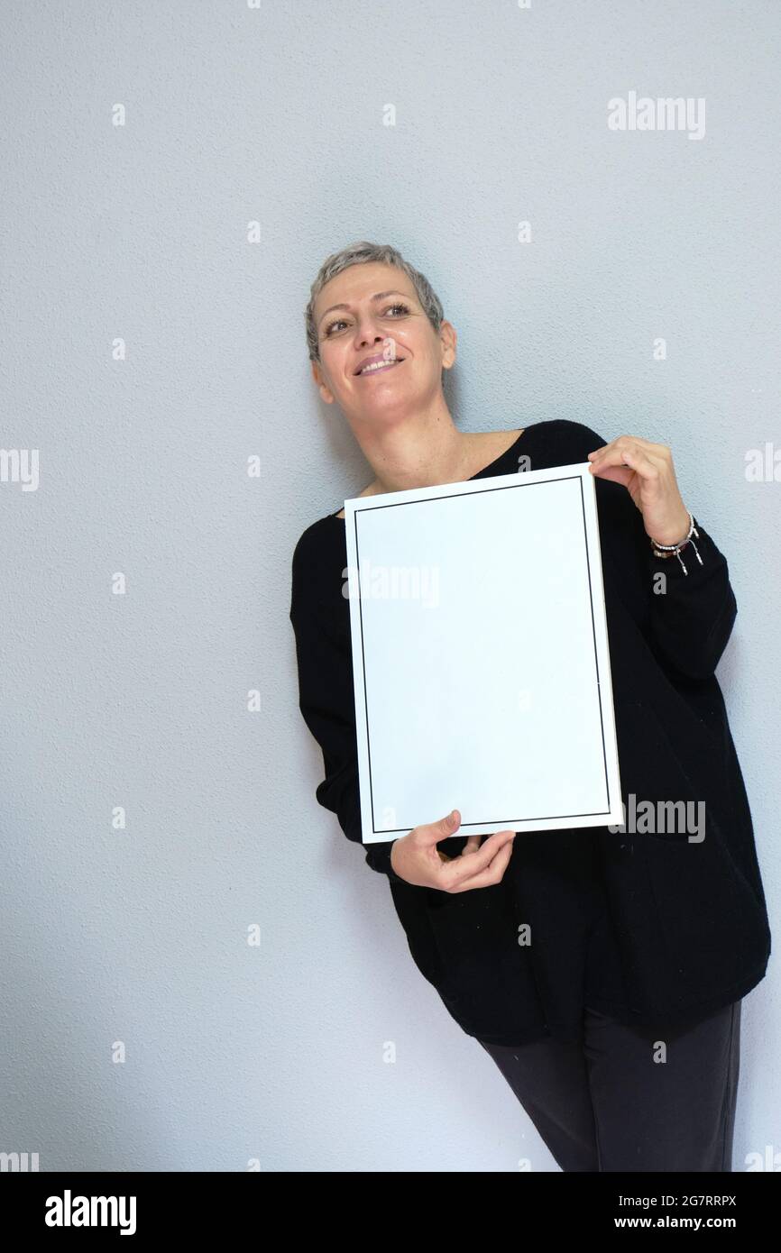 Closeup portrait of smiling attractive adult caucasian woman with gray hair looking at camera  holding empty  blank frame. Isolated view on grey backg Stock Photo