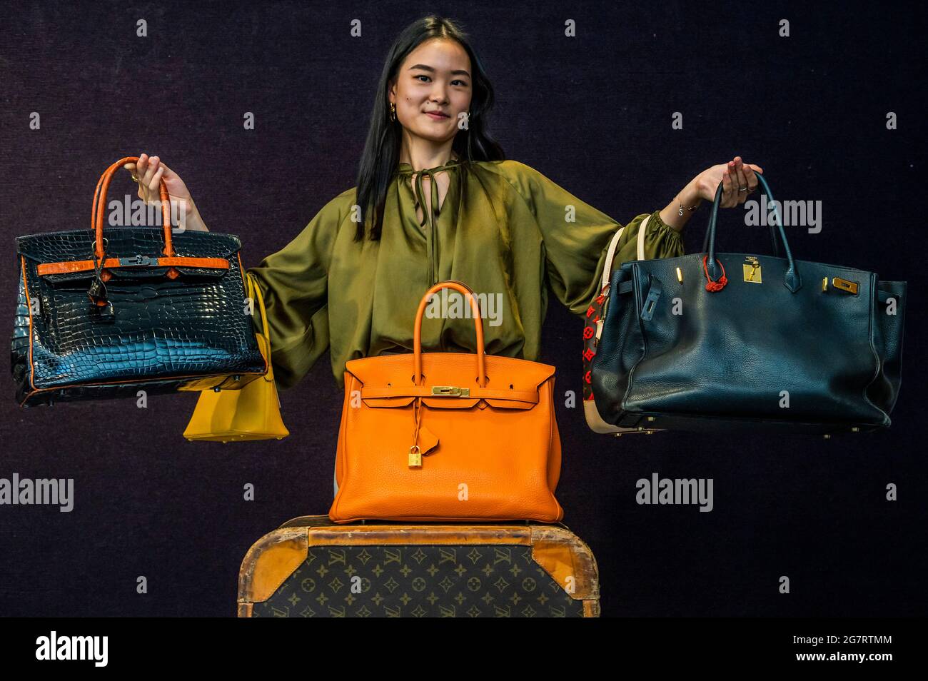 London, UK. 16th July, 2021. Black and Orange H Shiny Crocodile Birkin 35, Hermès, Limited edition 2007, est £18,000-22,000 (L) with Jane Birkin's Black Togo Birkin 35, Hermès, c. 1999, est £15-20,000 (signed by her in Tipp-Ex on the interior and held by Suzi Yang, cataloguer, R) and other bags - Preview of Bonhams' Designer Handbags and Fashion sale at their Knightsbridge site. The sale takes place on Wednesday 20 July. Credit: Guy Bell/Alamy Live News Stock Photo