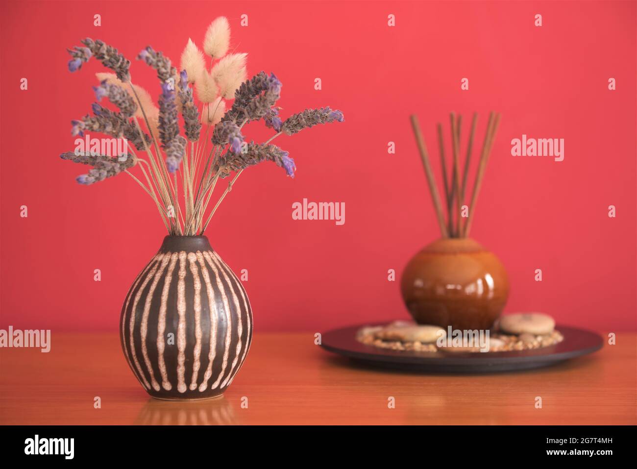 A vase of lavender and aroma diffusion sticks on a wooden table with a red background Stock Photo