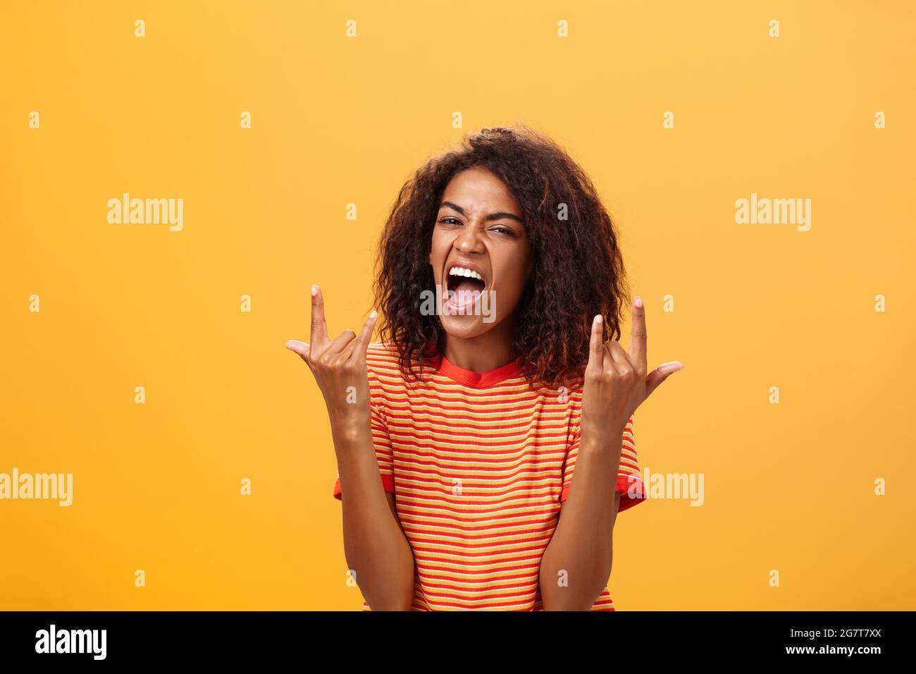 Waist-up shot of amazed happy stylish african american woman feeling awesome rocking on party yelling from joy and satisfaction showing rock n roll Stock Photo