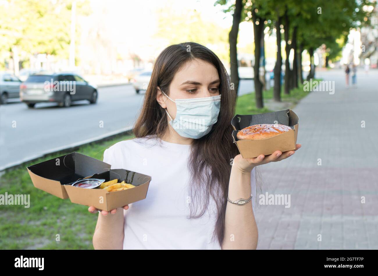 A masked woman deliverer of food during a pandemic and quarantine keeps ...