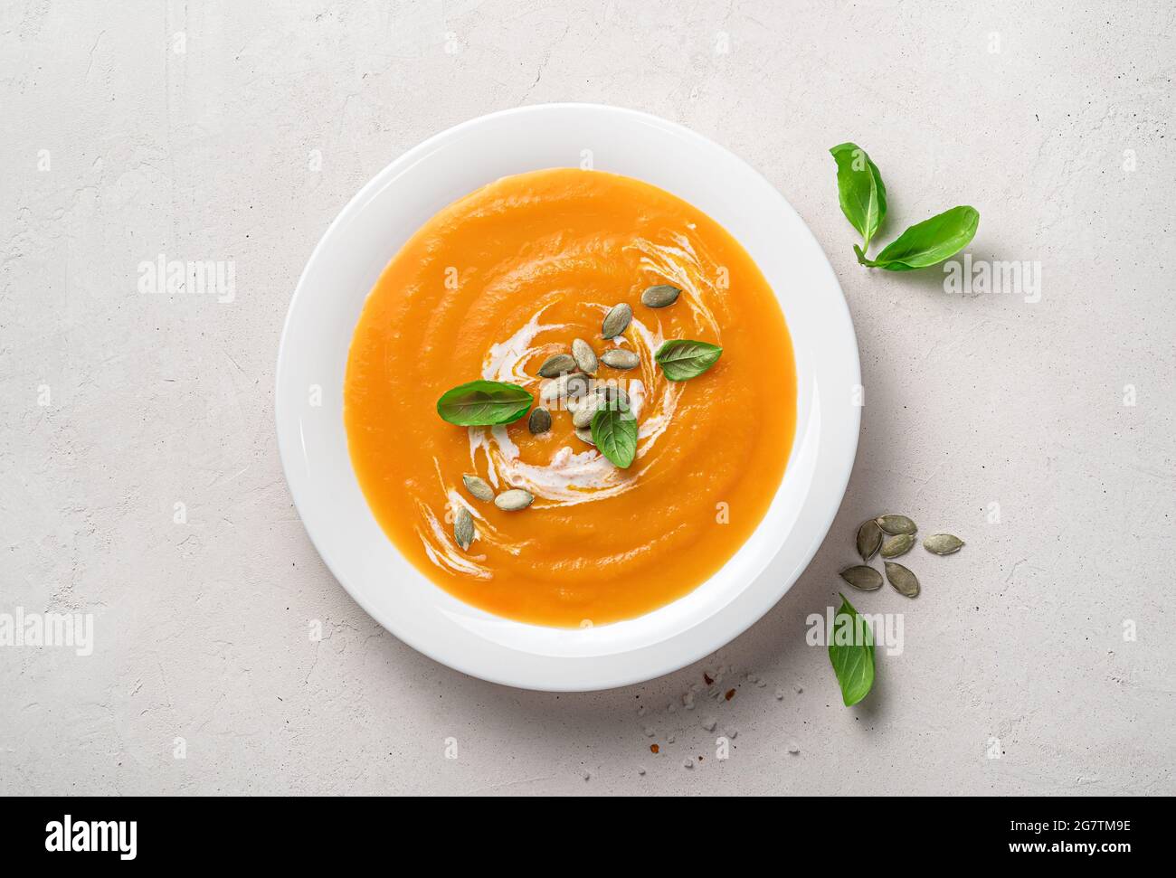 Pumpkin cream soup with basil, cream and pumpkin seeds on a gray background. Stock Photo