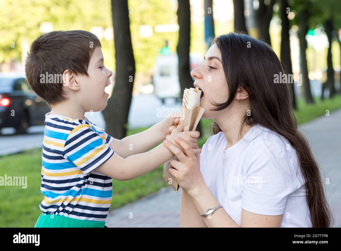 A baby boy feeds his mother a shaurma in the street. Advertising fast food and street food. Stock Photo
