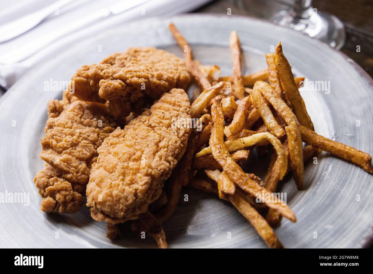 A plate of chicken tenders and thin skinny golden french fries on a