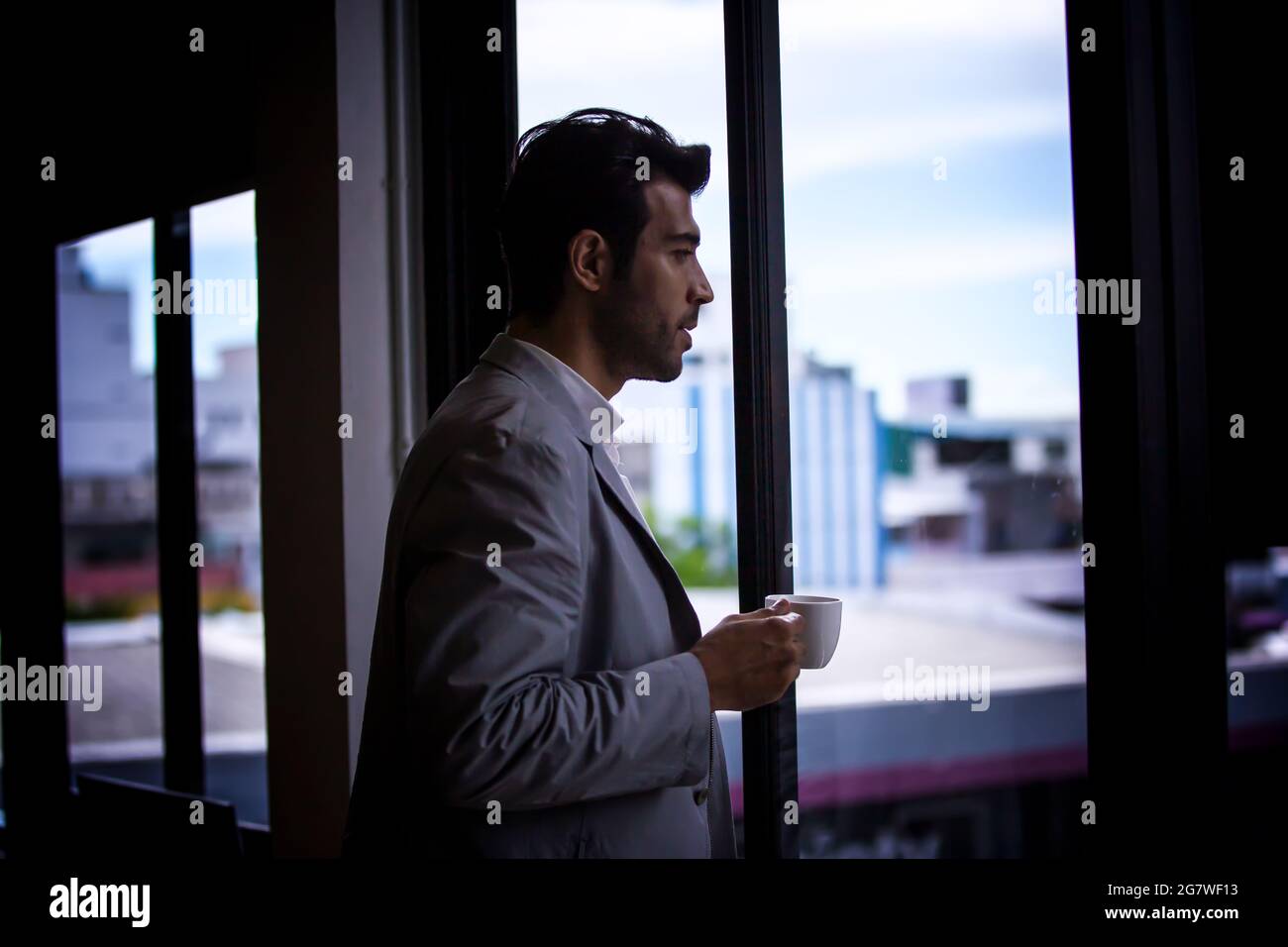 businessman drinking coffee while standing by window. Stock Photo