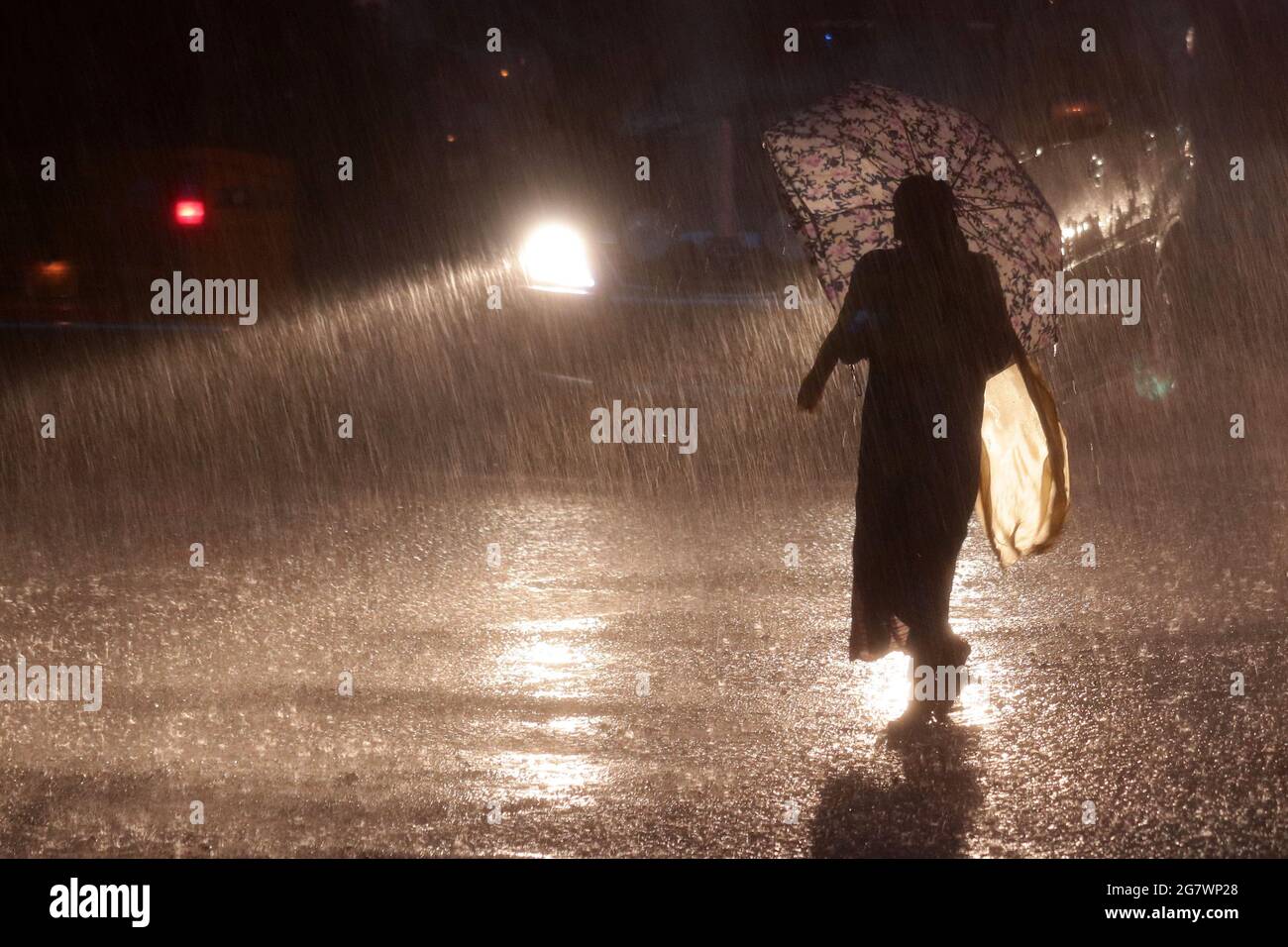 Chennai, Tamil Nadu, India. 16th July, 2021. During a heavy rainstorm, a woman takes shelter under an umbrella while walking down a street in Chennai. Credit: Sri Loganathan/ZUMA Wire/Alamy Live News Stock Photo