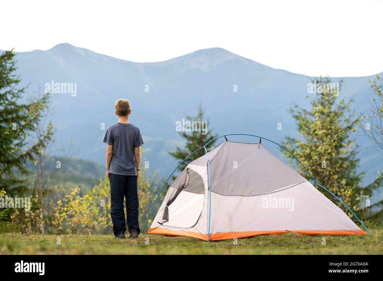 Hiker child boy standing near a tent in mountain campsite enjoying view ...