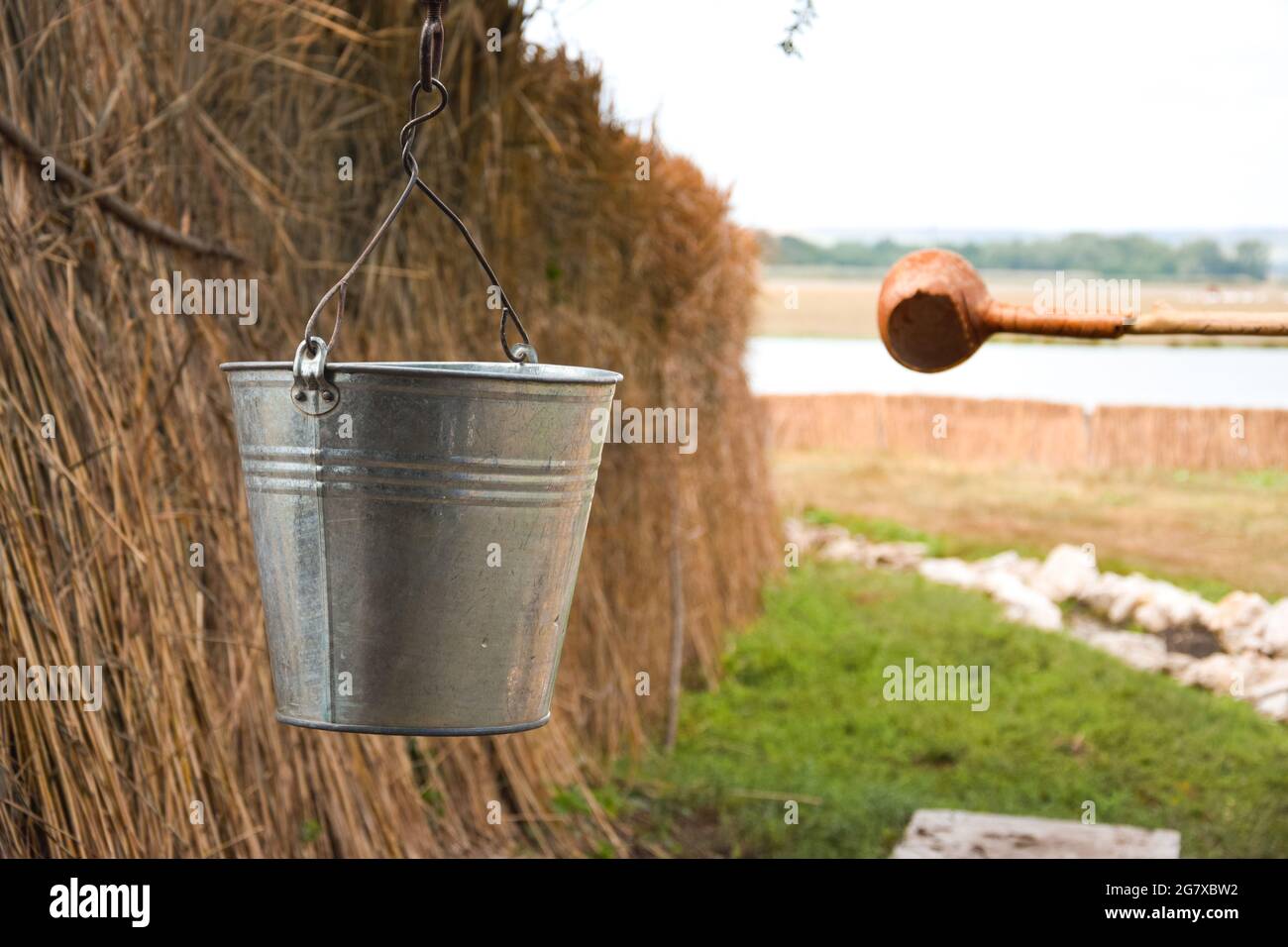 A water fountain with an old bucket and a makeshift mug made of pumpkin. Reed fence in background. Rural concept in the village. Traditions and lifest Stock Photo