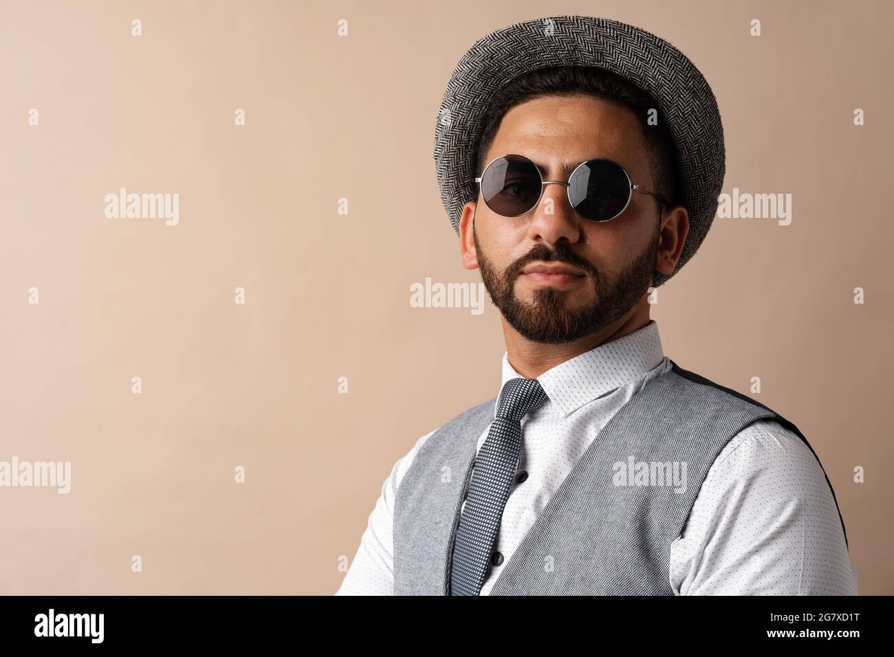 Cool egyptian man in hat and sunglasses posing against beige background