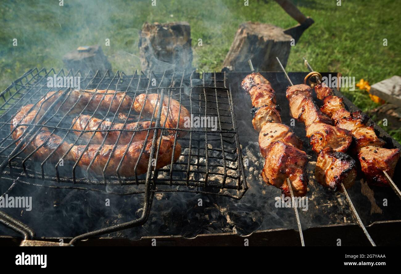 Barbeque meat and sausages or bratwurst on a grill grate in backyard. Man preparing shashlik or shish kebab over charcoal. Grilled meat on metal Stock Photo