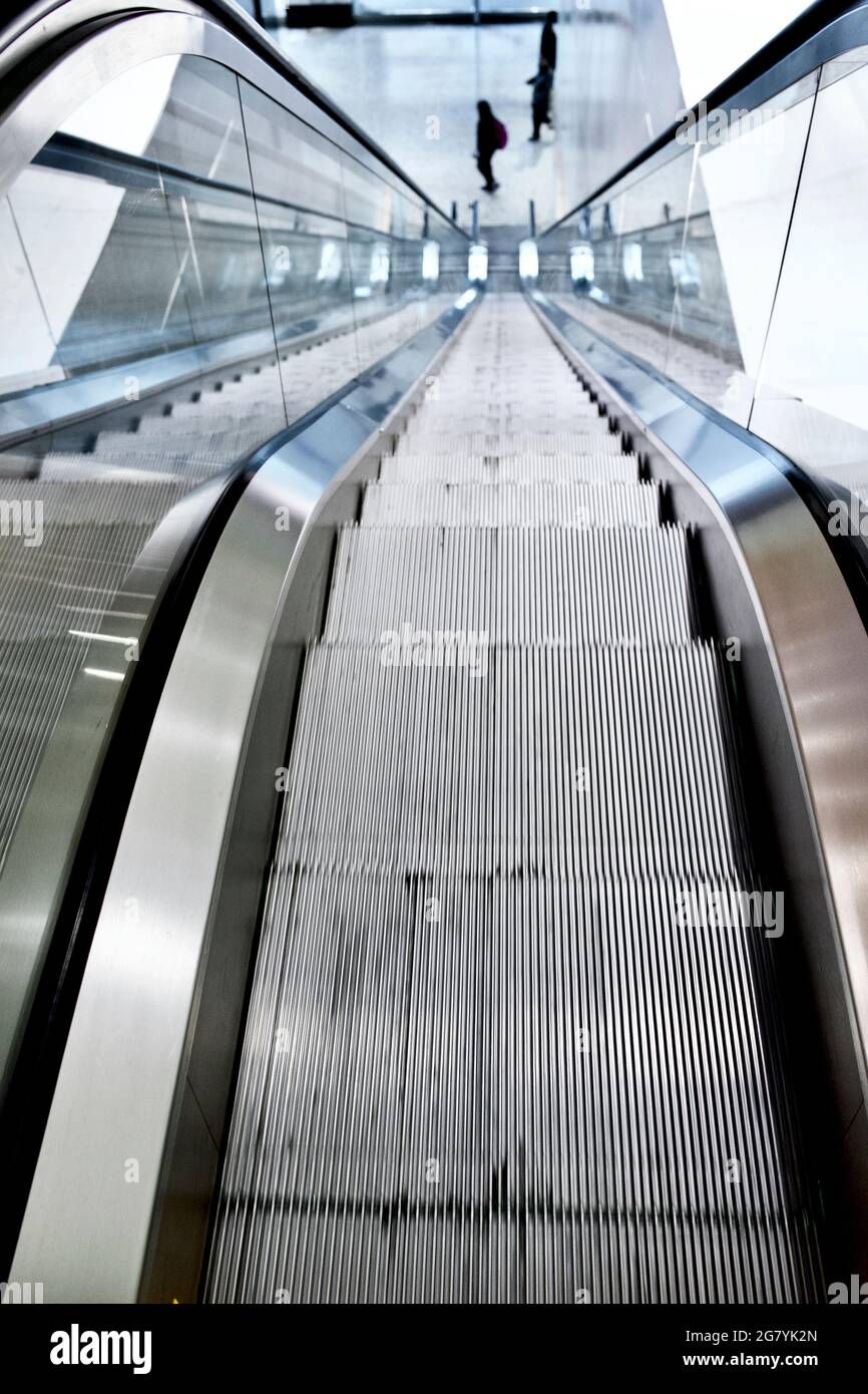 Escalator in office building with three people, strong perspective lines, looking down. Stock Photo