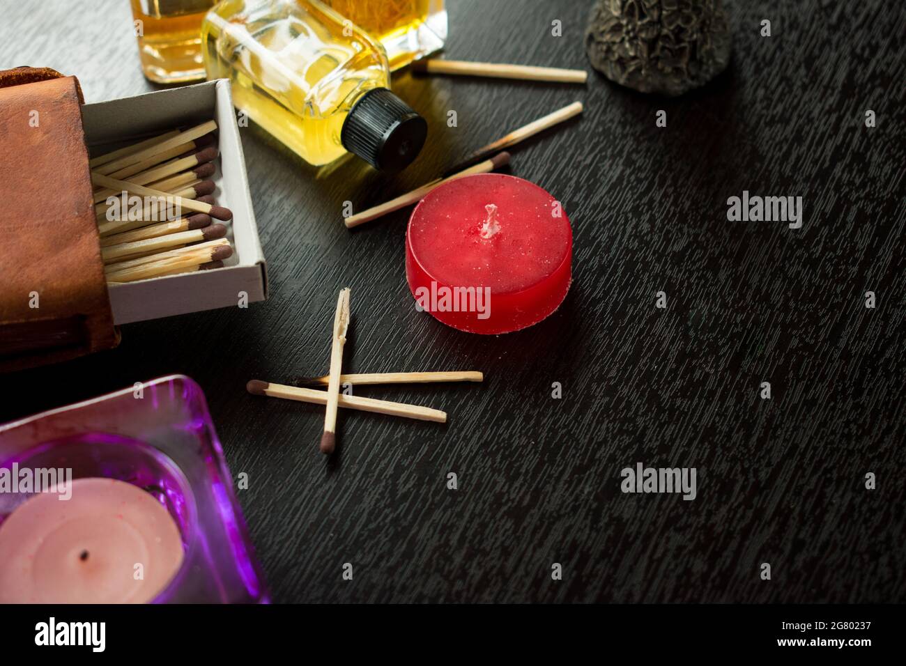 Some wooden matches in a matches box, candles and some glass flovering bottles on a black wooden table Stock Photo