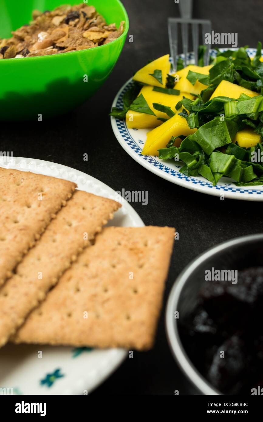 Healthy mango and spinach salad, soda cookies and some prunes on a black wooden table Stock Photo