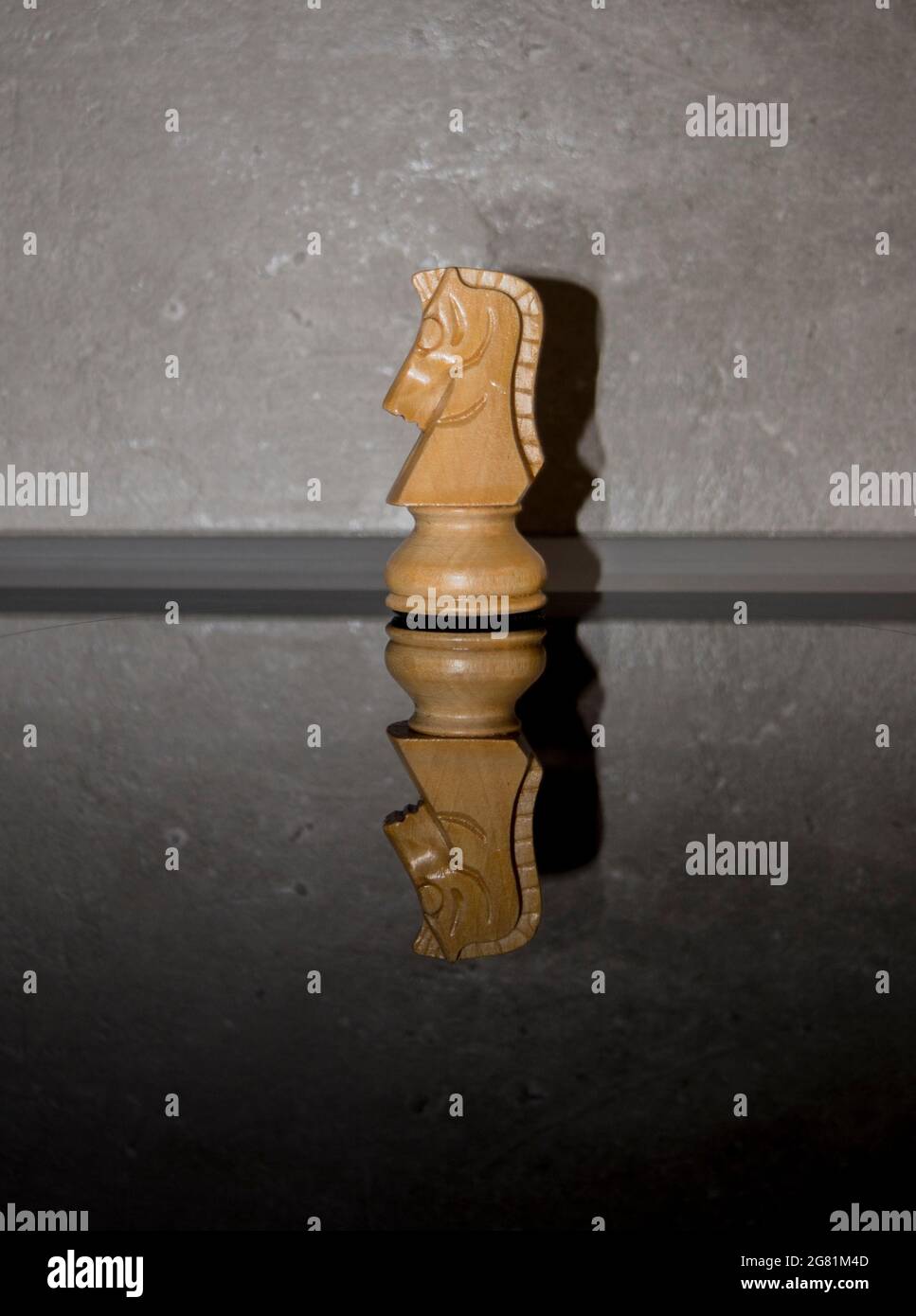Wooden white chess piece, knight on dark mirror glass with concrete wall background. Games, sports and recreation idea. Stock Photo
