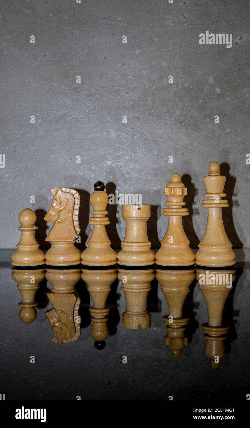 Wooden white chess pieces on dark mirror glass with concrete wall background. Games, sports and recreation idea. Minimal intelligence concept. Stock Photo