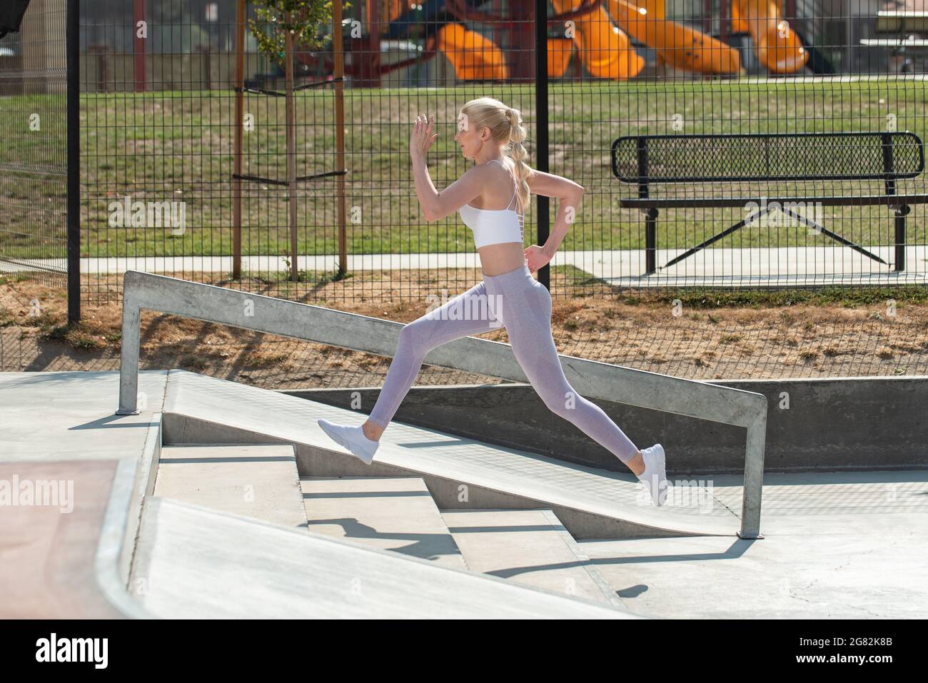 Healthy and fit atrractive blonde woman leaping up a short flight of concrete stairs at the park. Stock Photo