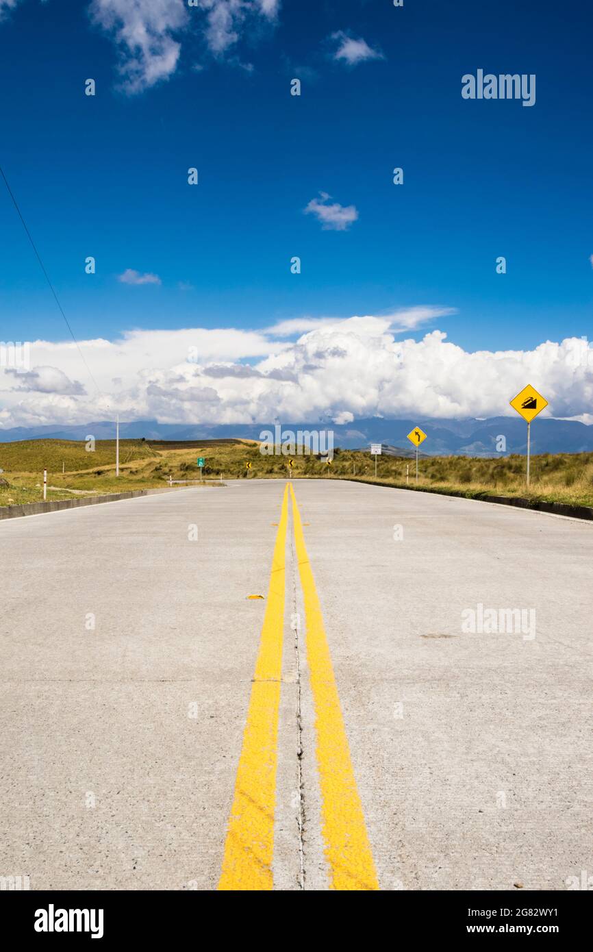 Highway in the mountains with a blue sky with some clouds. Street signs that indicate a curve. Stock Photo